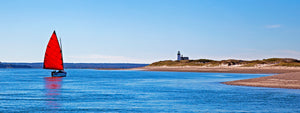 Catboat sailboat with red sail drifting by Sandy Neck lighthouse and sand dunes on Barnstable Harbor, Cape Cod. Art Gallery featuring fish prints, coffee mugs, towels and blankets inspired by the sea and sand by artist Charles Harden of Cape Cod.